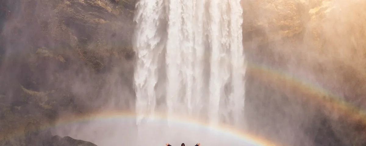 A man standing under a rainbow at a waterfall